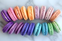 Colorful French macarons arranged in rainbow pattern on marble background, featuring purple, pink, orange, blue, turquoise and mint green delicate pastries.