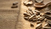 Sunflower seeds scattered on natural burlap fabric with wooden spoon and bowl, suitable for food photography, healthy snacking, nutrition content, and culinary styling projects.
