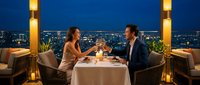 Elegant couple enjoying romantic dinner on luxury rooftop terrace with city skyline view at night. Fine dining restaurant atmosphere with candles and wine.