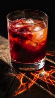 Dark red berry cocktail with ice in a rocks glass on rustic wood, dramatic moody lighting with glowing orange reflections on the surface.