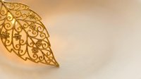 Golden ornate leaf with intricate filigree patterns on warm beige background for luxury design projects and decorative applications.