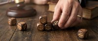 Hand placing wooden dice with justice scales symbols on rustic table for legal gambling concept. Law enforcement and judicial decision making theme.