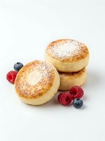 Fluffy baked pastries dusted with powdered sugar, garnished with fresh raspberries and blueberries on white background for bakery and food styling.