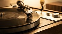 Vintage turntable with vinyl record spinning in warm golden light. Classic audio equipment for music production, DJ mixing, and retro sound system setup.