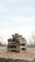 Balanced stack of weathered driftwood and smooth stones creating zen meditation tower on sandy beach surface with soft blurred coastal background.