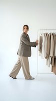 Young Caucasian woman fashion stylist selecting neutral tone clothes from rack in minimalist studio for wardrobe styling and personal shopping services.