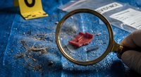 Crime scene investigation with magnifying glass examining blood evidence on blue surface with forensic markers and documentation materials.