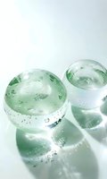 Glass spheres with water drops casting soft shadows on white surface. Transparent orbs with condensation create minimalist composition in mint green tones.