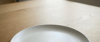 Empty white ceramic plate on light wooden table surface, suitable for food photography, restaurant menus, and culinary design projects.