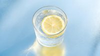 Refreshing glass of sparkling lemon water with ice and fresh citrus slice on blue background, perfect for beverage, wellness and lifestyle design projects.