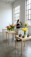 Female florist arranging colorful tulips and flowers on wooden tables in bright modern studio with large windows and white brick walls.