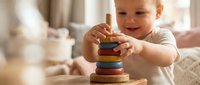 Adorable toddler boy playing with colorful wooden stacking rings toy in bright nursery room. Educational development activity for early childhood learning.