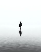 Mysterious silhouette of person standing on water surface with reflection against foggy minimalist background, creating surreal atmospheric scene.