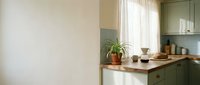Modern kitchen with sage green cabinetry, wooden countertop, potted plant, and natural light from window. Minimalist interior design for home decor and lifestyle content.