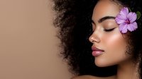 Young African American woman with natural curly hair and purple hibiscus flower, eyes closed in serene expression against neutral background, glowing skin and pink lips.