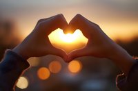 Hands forming heart shape silhouette against golden sunset with bokeh lights creating romantic atmosphere for love and connection concepts.