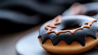 Chocolate glazed donut with black frosting and orange bat-shaped decoration on dark background, macro food photography for Halloween season treats.
