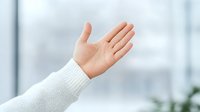 Open palm gesture showing empty hand in white sweater sleeve against blurred light background, representing welcome, presentation or business communication concept.