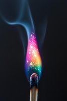 Burning match with magical rainbow colored flame and sparkling particles against dark background. Smoke trails create ethereal atmosphere. Macro photography.