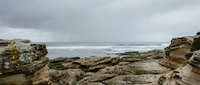 Rugged rocky coastline with dramatic stone formations and turbulent ocean waves under overcast sky, suitable for travel and nature backgrounds.
