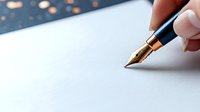 Hand holding elegant fountain pen writing on clean white paper with warm bokeh lights creating atmospheric background for creative writing projects.