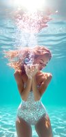 Young woman in sparkling swimsuit underwater blowing bubbles, with floating red hair and dreamy expression in turquoise pool water with sunlight streaming.