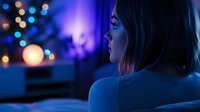 Young woman relaxing at home in evening with colorful bokeh lights creating cozy atmosphere for holiday season and winter comfort lifestyle.