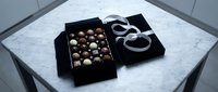 Luxury chocolate assortment in black gift box with white ribbon on marble surface, premium confectionery packaging for special occasions and gourmet gifting.
