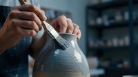 Potter hands shaping clay vessel on wheel with sculpting tool in ceramic studio workshop for handmade pottery creation and artistic craftsmanship.