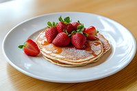 Stack of fluffy pancakes topped with fresh strawberries, maple syrup and powdered sugar served on white plate, close up view on wooden table background.