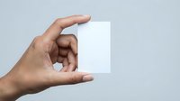 Hand holding a blank white card mockup on a light gray background, ready for custom text or logo design.