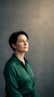 Professional businesswoman in green silk blouse looking confidently ahead with determined expression against neutral studio background for corporate branding.