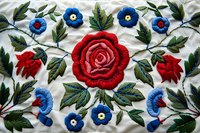 Traditional floral embroidery pattern with vibrant red roses and blue flowers on white fabric, featuring detailed green leaves and decorative stitching in folk art style.