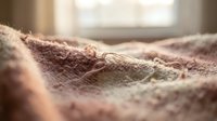 Cozy knitted blanket texture in soft pink tones with warm natural lighting creating comfortable home atmosphere for relaxation and comfort concepts.
