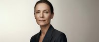 Confident mature Caucasian businesswoman in dark blazer posing against neutral background, conveying authority and professionalism.
