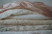 Stack of soft bedding with white pillows, floral pattern duvet, and pink satin sheet, creating a cozy and elegant bedroom atmosphere.