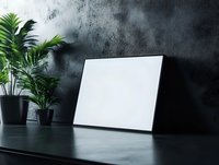 Blank white canvas leaning against dark textured wall with potted green plants on black table, mockup for artwork display or design presentation.