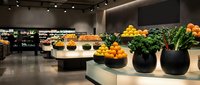 Modern grocery store produce section with fresh fruits and vegetables displayed in sleek black bowls on white curved counters under contemporary lighting.