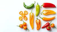 Colorful assortment of fresh hot chili peppers and sliced varieties arranged on white background for culinary and cooking projects.