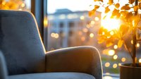 Cozy armchair by window at sunset with warm golden bokeh lights and houseplant creating peaceful atmosphere for relaxation and mindfulness moments.