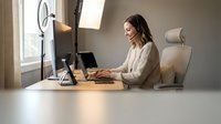Young professional woman working from home office setup with ring light and laptop for video calls and content creation.