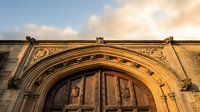 Historic stone church entrance with ornate Gothic arched doorway and decorative carved details against dramatic sunset sky for architectural design projects.