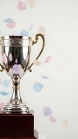 Silver trophy cup with ornate handle on wooden base surrounded by colorful confetti petals celebrating victory achievement success competition winner.