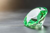Brilliant emerald green crystal gemstone on gray background with soft reflection and dramatic lighting. Luxury jewelry concept with copy space.