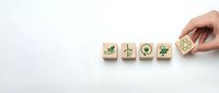 Hand placing wooden blocks with green eco icons including leaf, wind turbine, solar panel, and recycling symbol on white background, sustainability concept.