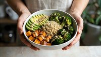 Person holding bowl with quinoa, roasted vegetables, avocado and broccoli. Healthy meal prep and nutritious eating concept for diet and wellness.