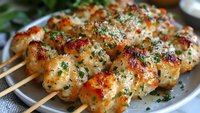Grilled chicken meatballs on wooden skewers with herbs and spices, served on white plate. Appetizer for barbecue party or restaurant menu.