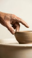 Skilled potter shaping wet clay bowl on spinning wheel, close-up of clay-covered hands crafting handmade ceramic pottery in studio.