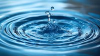 Single water drop falling into calm blue water creating concentric ripples and splash crown with floating droplets, captured in macro photography against dark background.