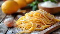 Fresh homemade pasta with raw egg and lemons on rustic wooden background, selective focus on traditional Italian spaghetti noodles dusted with flour.